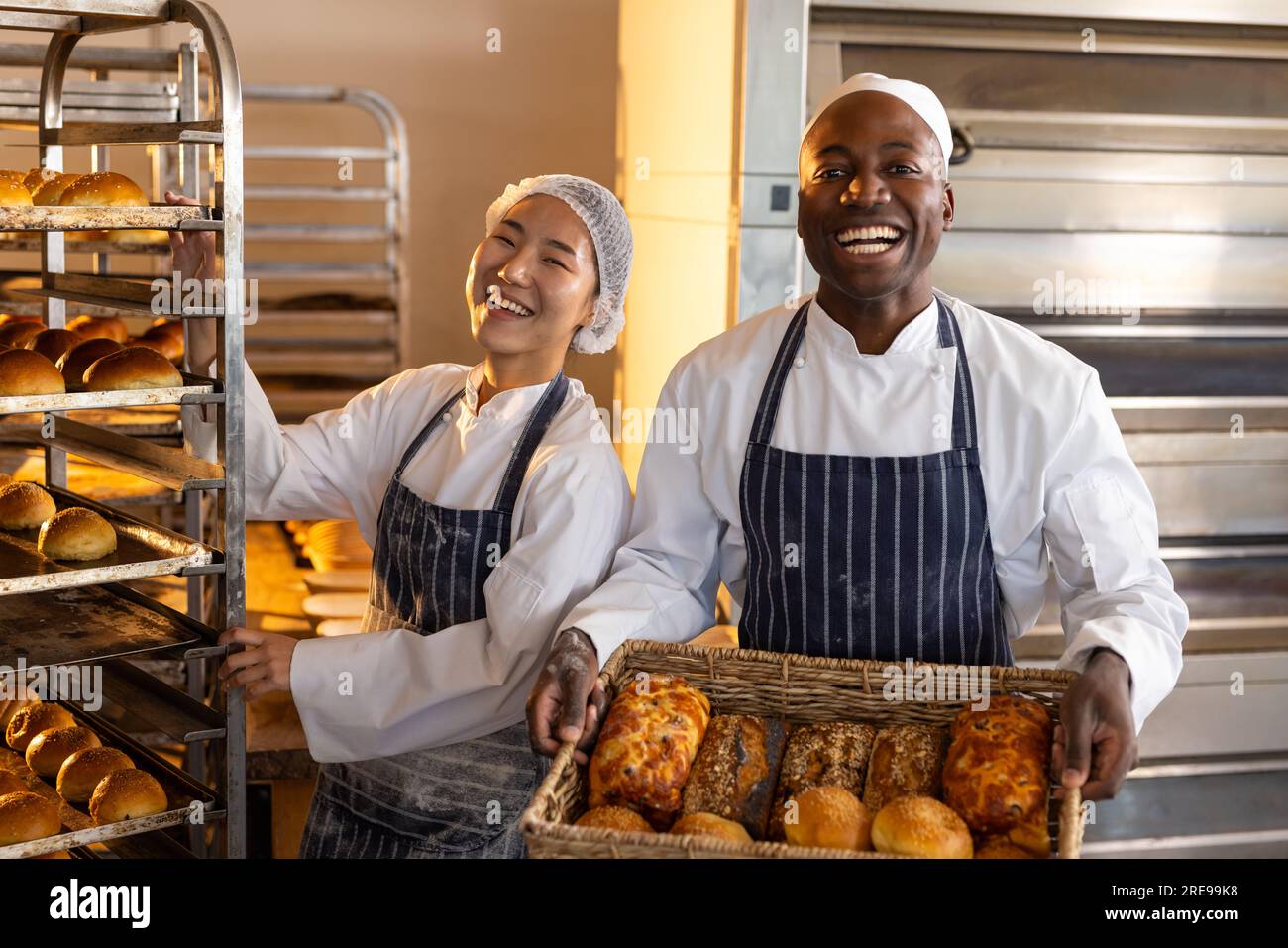 Portrait of happy diverse bakers wearing aprons in bakery kitchen and
