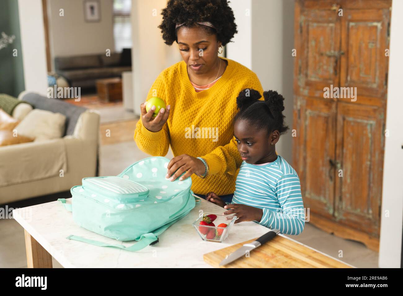 Happy african american mother and daughter packing lunch for school in kitchen at home Stock Photo
