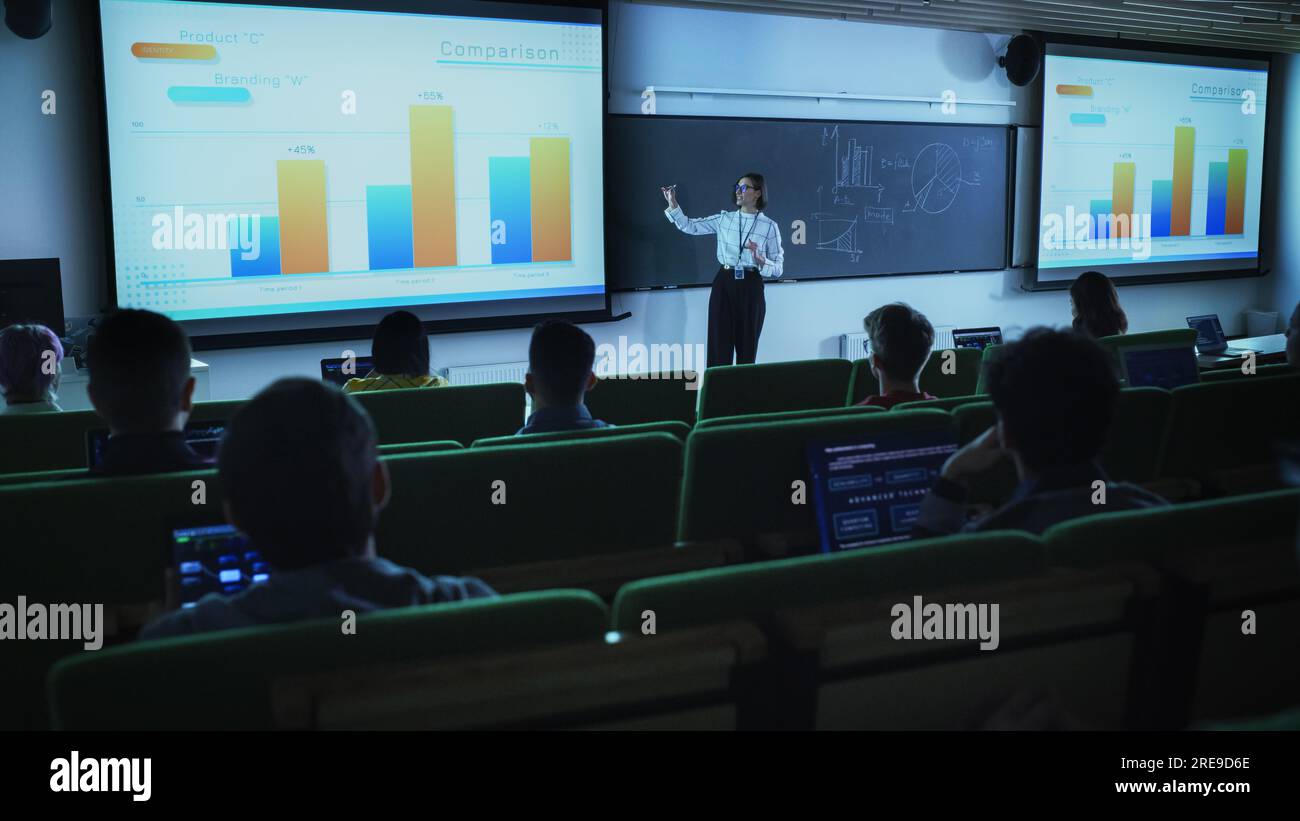 Young Female Teacher Giving a Data Science Lecture to Diverse Multiethnic Group of Female and Male Students in Dark College Room. Projecting Slideshow Stock Photo