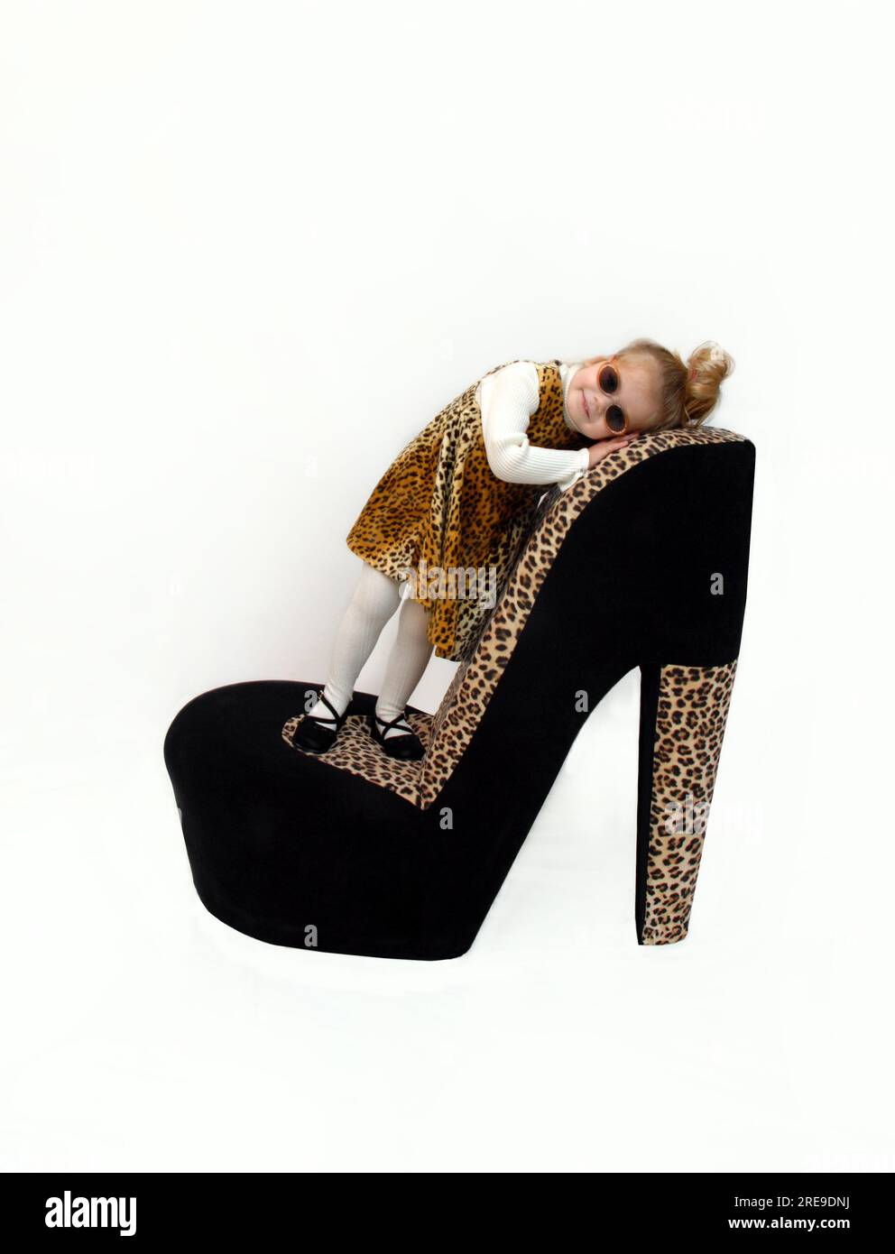 Little Girl models an animal print jumper and tights.  She has on sunglasses and is standing on a giant high heel shoe. Stock Photo