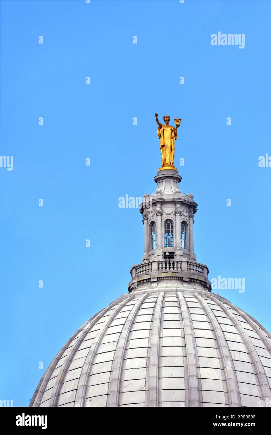 Cupola, of the Capitol of Wisconsin in Madison, is topped with golden figure.  Blue sky surrounds roof. Stock Photo