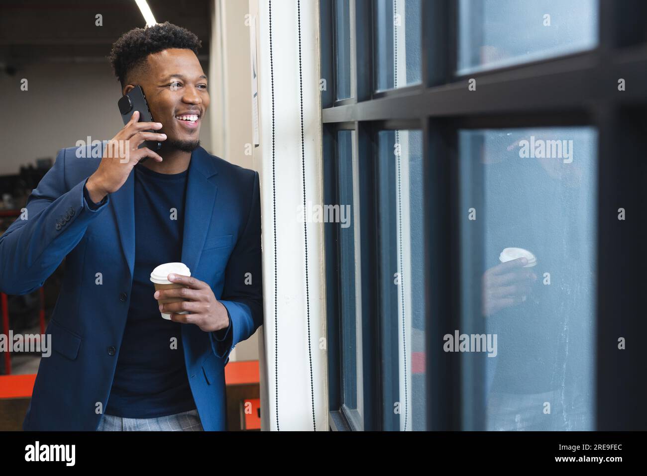 Happy african american man talking on smartphone while looking out of the window at office Stock Photo