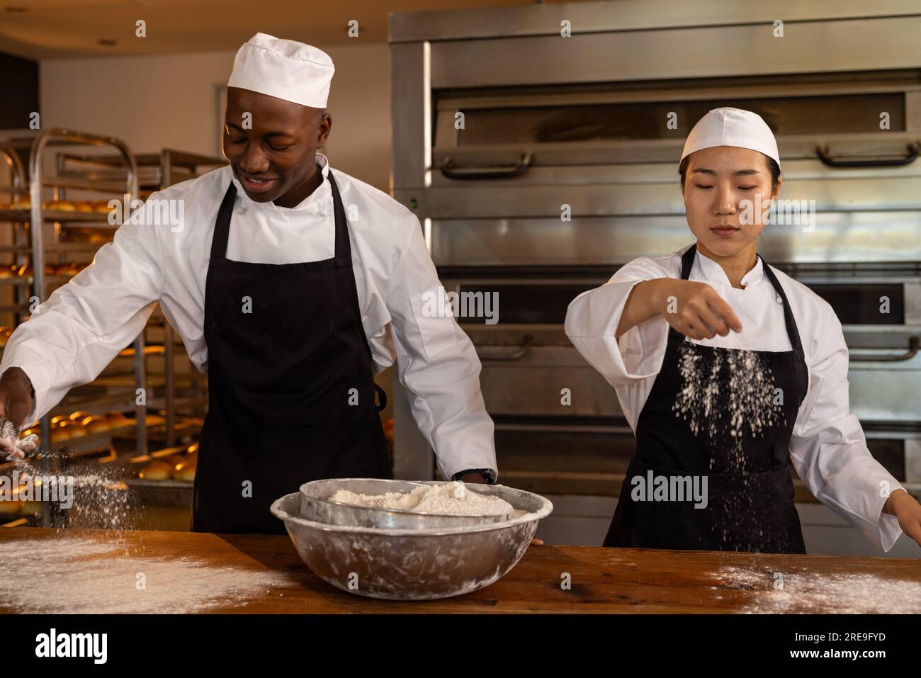 Happy diverse bakers working in bakery kitchen, pouring flour and