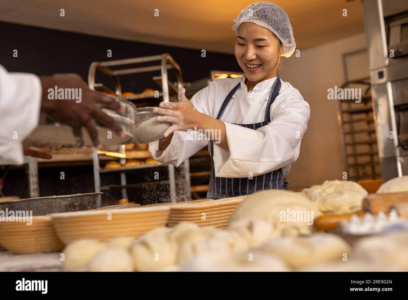 Happy diverse bakers wearing aprons in bakery kitchen and pouring flour