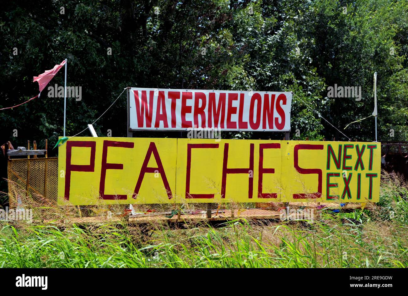 Large sign advertises peaches and watermelon for sale. Sign is attached