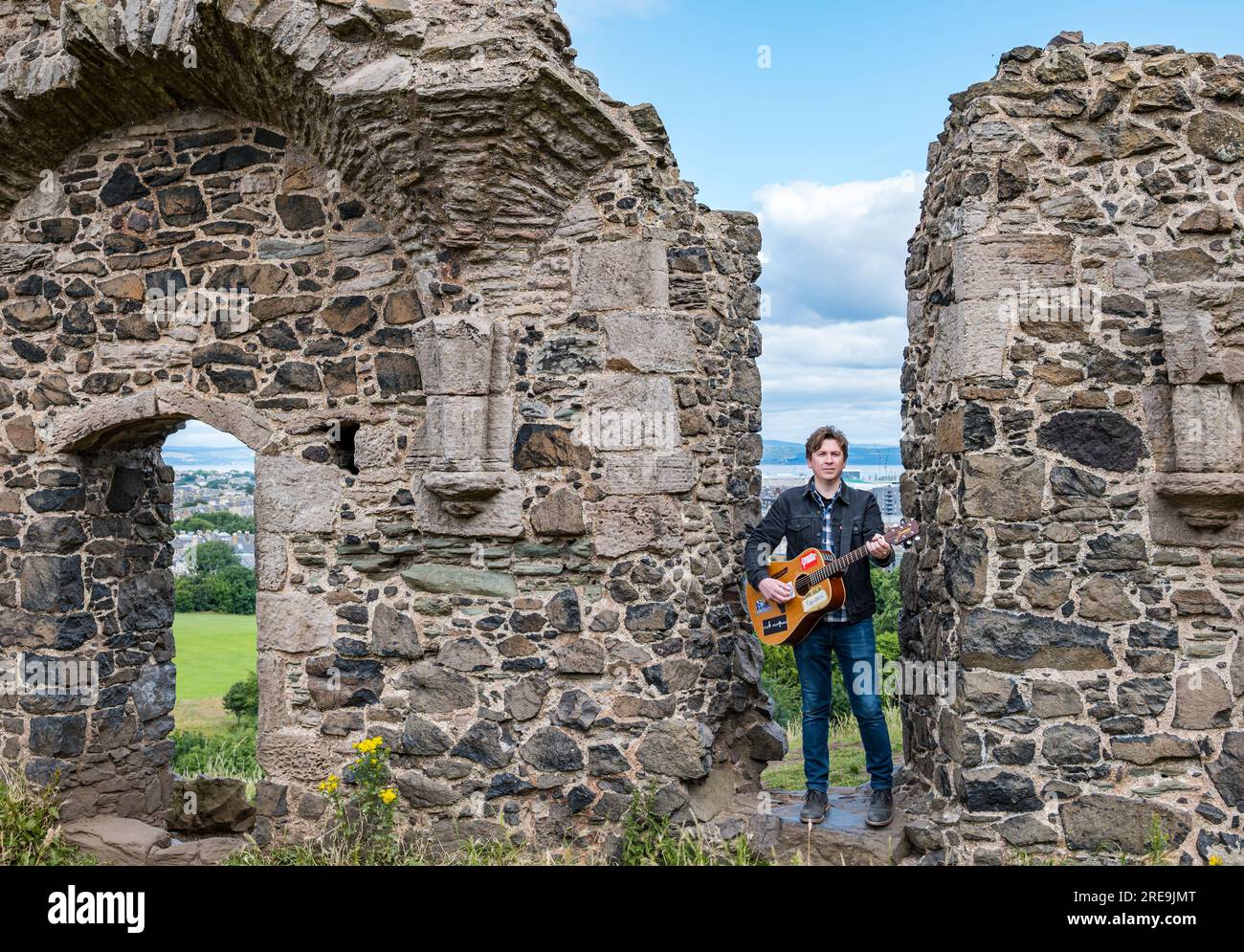 The Lonely Together musician Mike Baillie playing guitar at ruins of St Anthony's Chapel, Holyrood Park, Edinburgh, cotland, UK Stock Photo