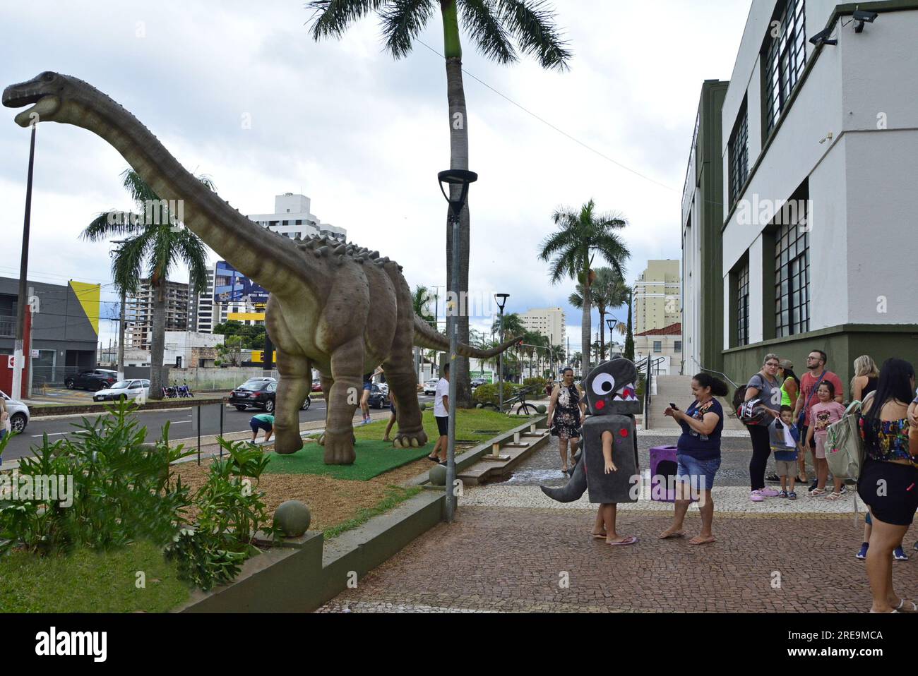 City: Marília, São Paulo, Brazil, April 04, 2023: People taking pictures in front of a replica of a dinosaur at the city's birthday party Stock Photo