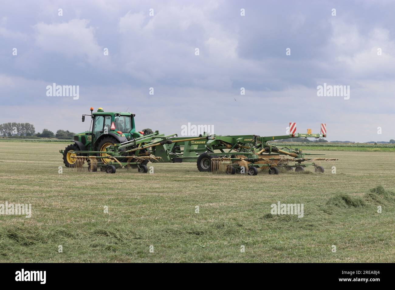 low angle view at a tractor with a big hay rake in a grass field in the ...