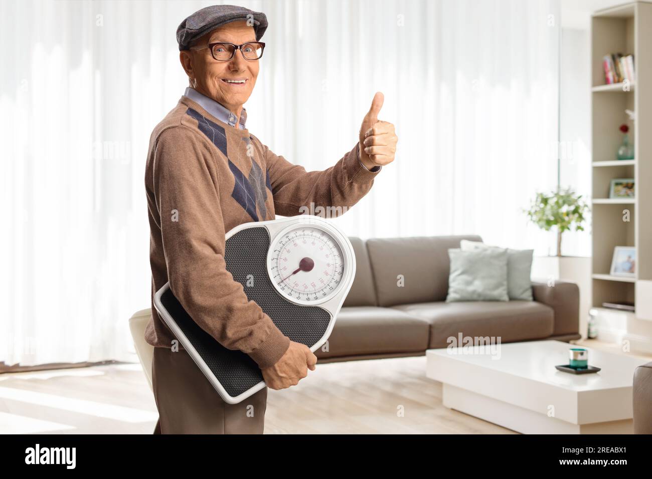 Elderly man holding a weight scale and gesturing thumbs up in a living