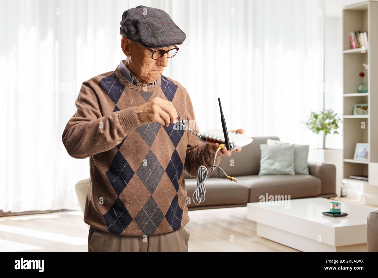 Elderly man fixing a router with a screwdriver at home in a living room ...