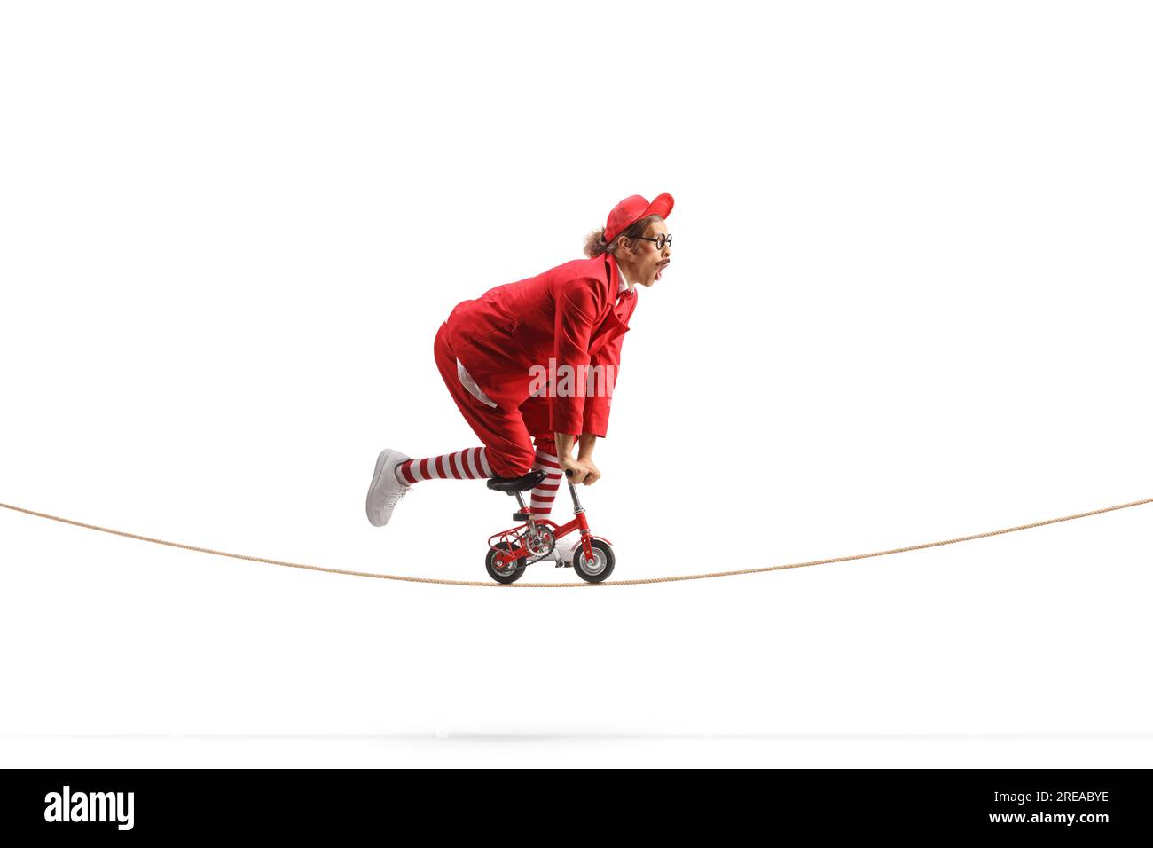 Entertainer in a red suit riding a small bike over a tightrope isolated on white background Stock Photo
