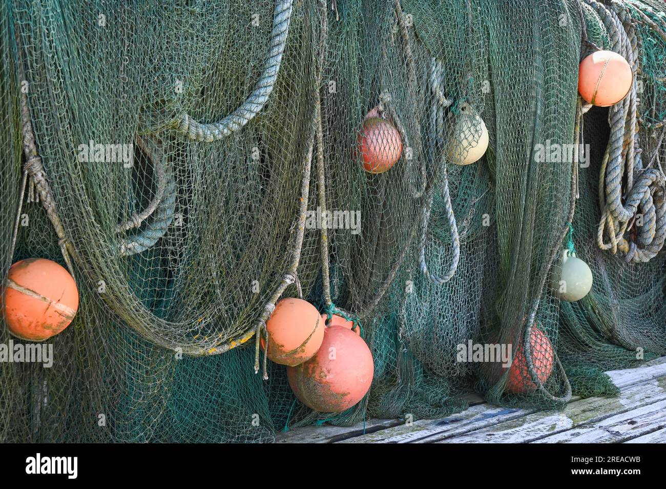 Fishing nets with orange buoy floaters laid out to dry on a pier. Stock Photo
