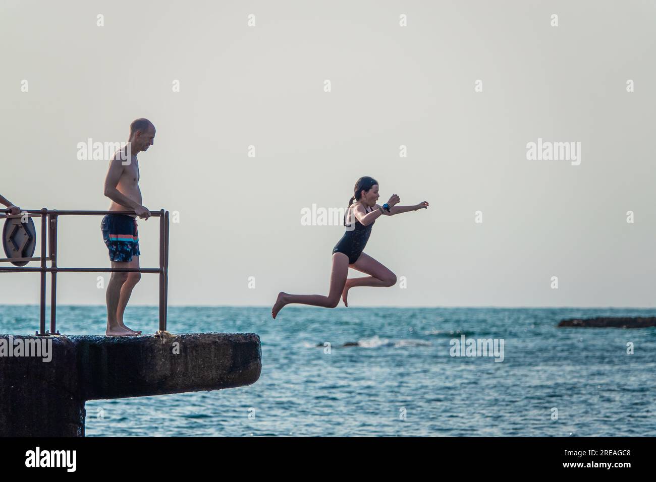 Young people jumping into the sea in a sunset on a beach in summer. Stock Photo