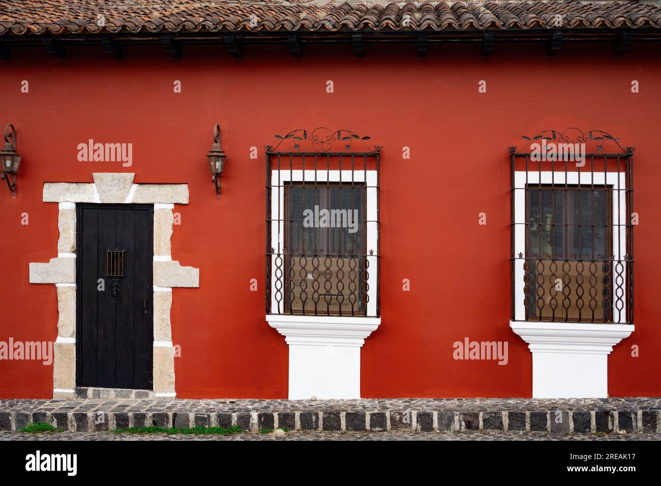 front door and windows with safety bars in a red painted small, old house in Guatemala Stock Photo