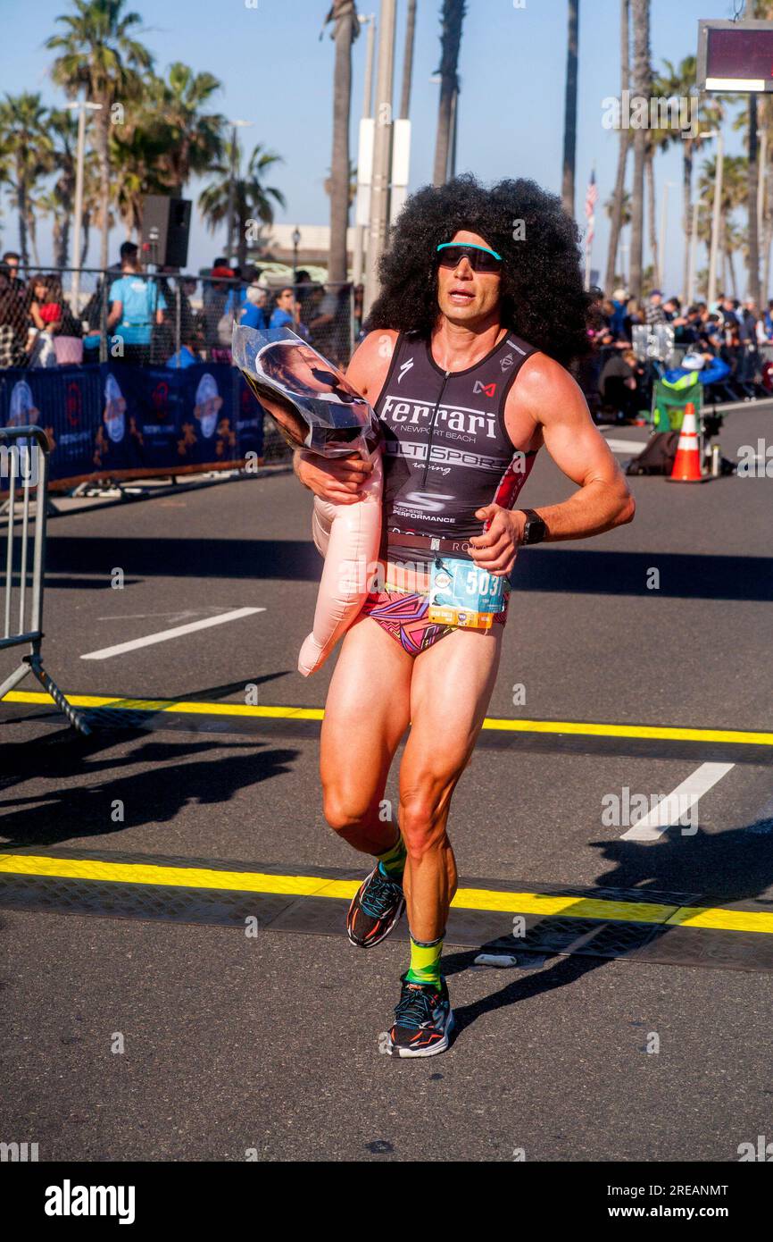 Huntington Beach, California, USA. 4th Feb, 2018. A marathon runner in Hunting Beach, CA, crosses the finish line wearing a fright wig and an inflated female figure, explaining cryptically that ''It's about the beach. (Credit Image: © Spencer Grant/ZUMA Press Wire) EDITORIAL USAGE ONLY! Not for Commercial USAGE! Stock Photo