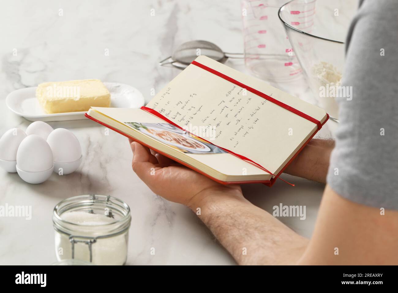 Man with recipe book at white marble table in kitchen, closeup Stock Photo