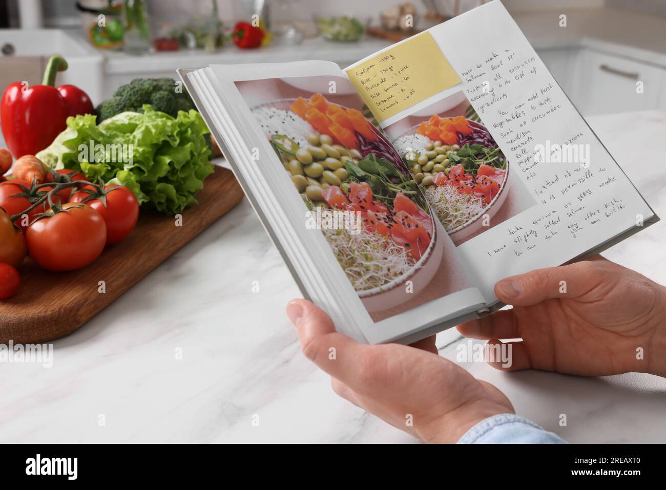 Man with recipe book at white marble table in kitchen, closeup Stock Photo