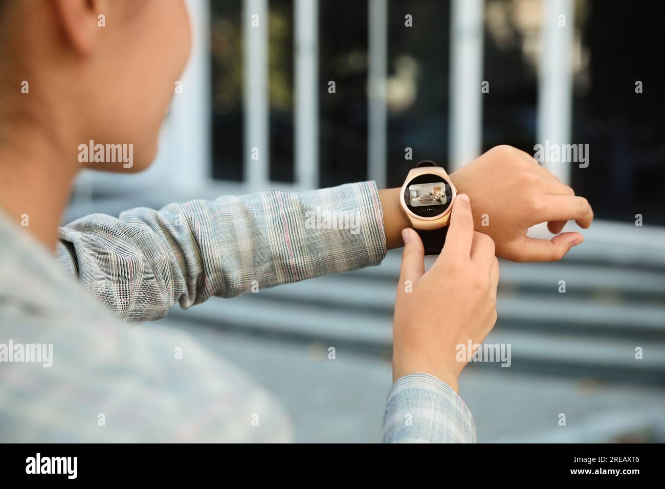 Woman checking home security system via smartwatch app outdoors, closeup. Image of room through CCTV camera on display Stock Photo