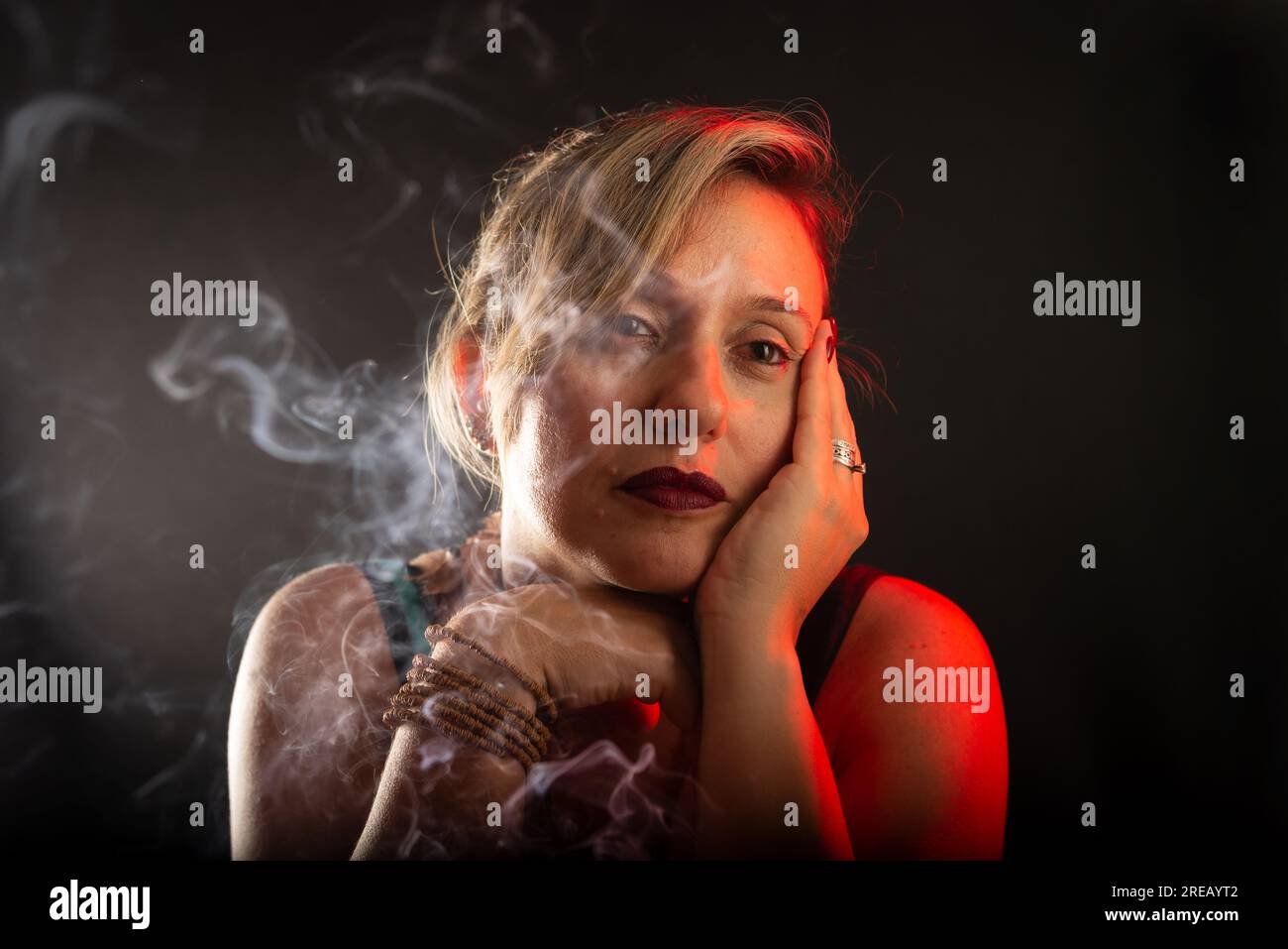 Attractive and beautiful woman with hand touching her face lightly. Incense smoke all around. Studio portrait. Isolated on a black background. Stock Photo