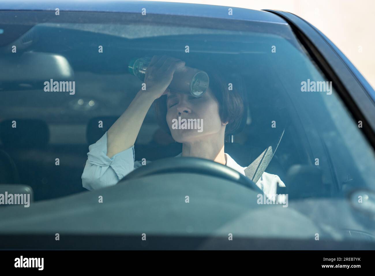 Suffering from heat exhausted woman driver sits in car put cold bottle to forehead with close eyes Stock Photo