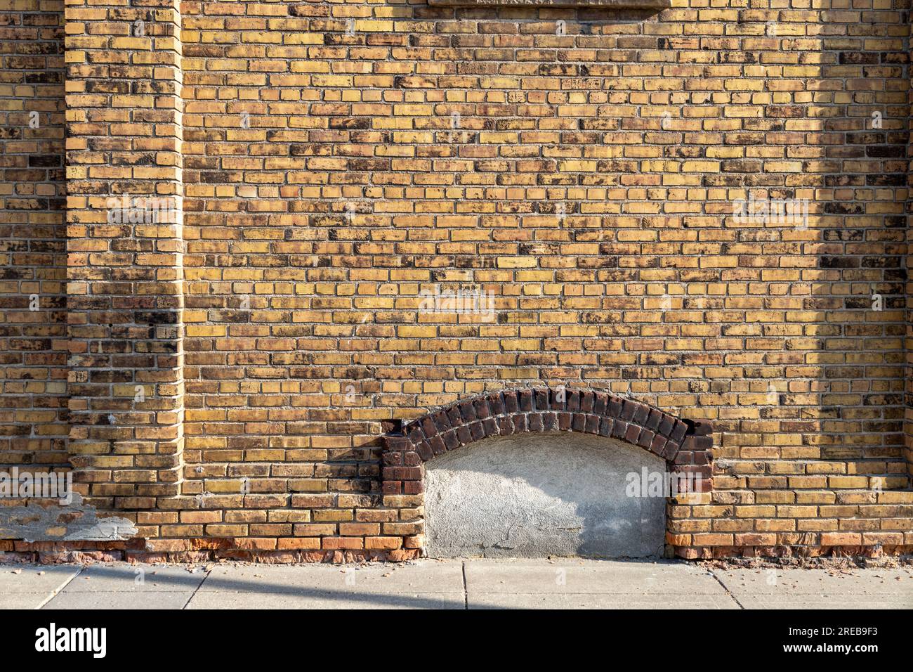 Full frame texture background of an attractive old mottled yellow and brown color brick wall, with view of an enclosed arched basement window Stock Photo