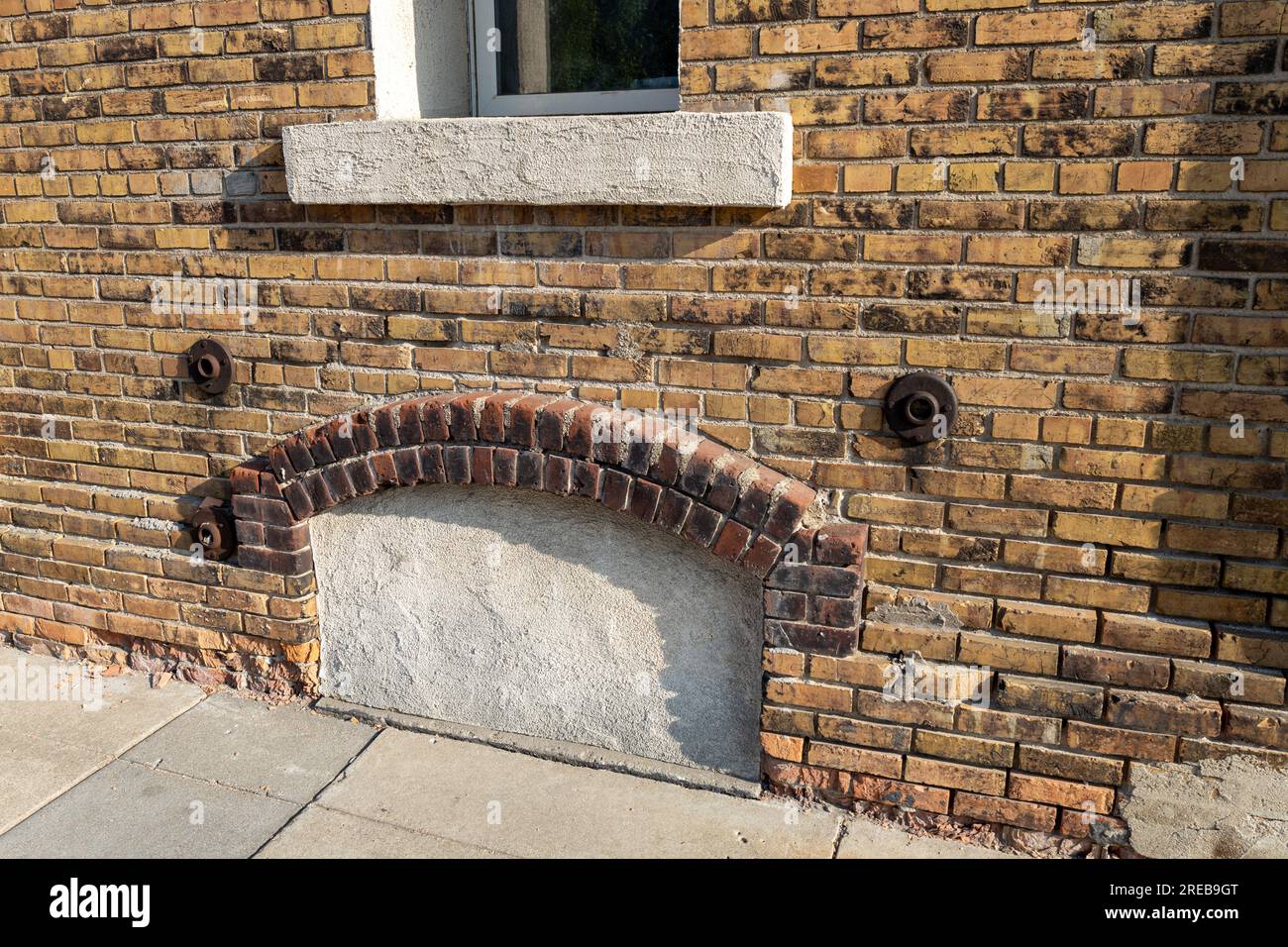 Full frame texture background of an attractive old mottled yellow and brown color brick wall, with view of an enclosed arched basement window Stock Photo