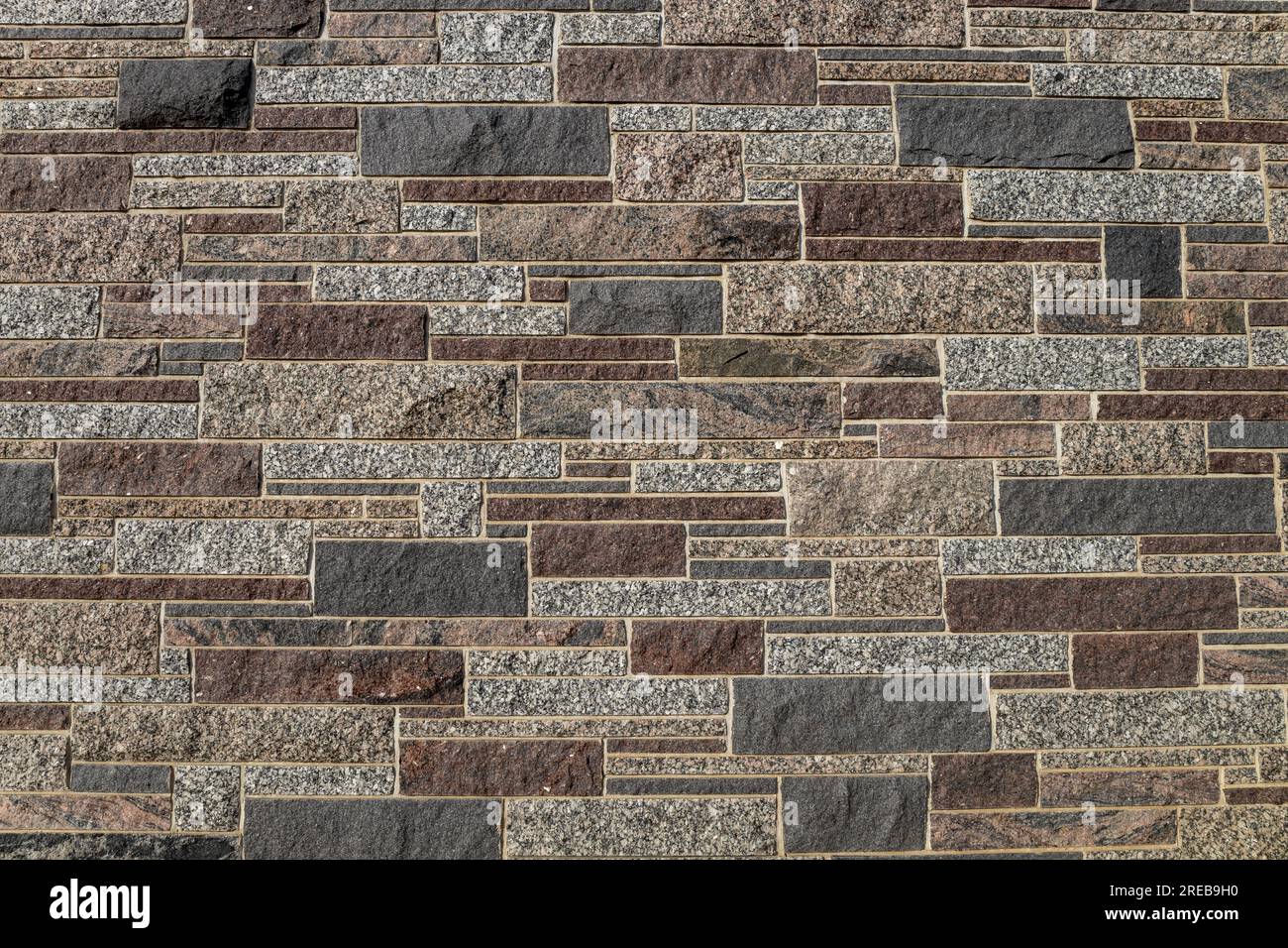 Full frame texture background of a modern granite stone wall in ashlar masonry style, in varying sizes and shades of white, brown, red and blue Stock Photo