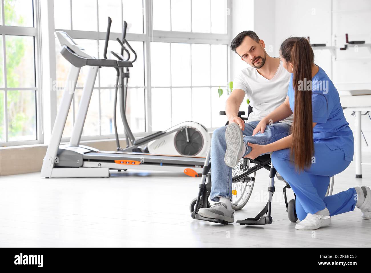 Female physiotherapist working with young man in wheelchair at rehabilitation center Stock Photo