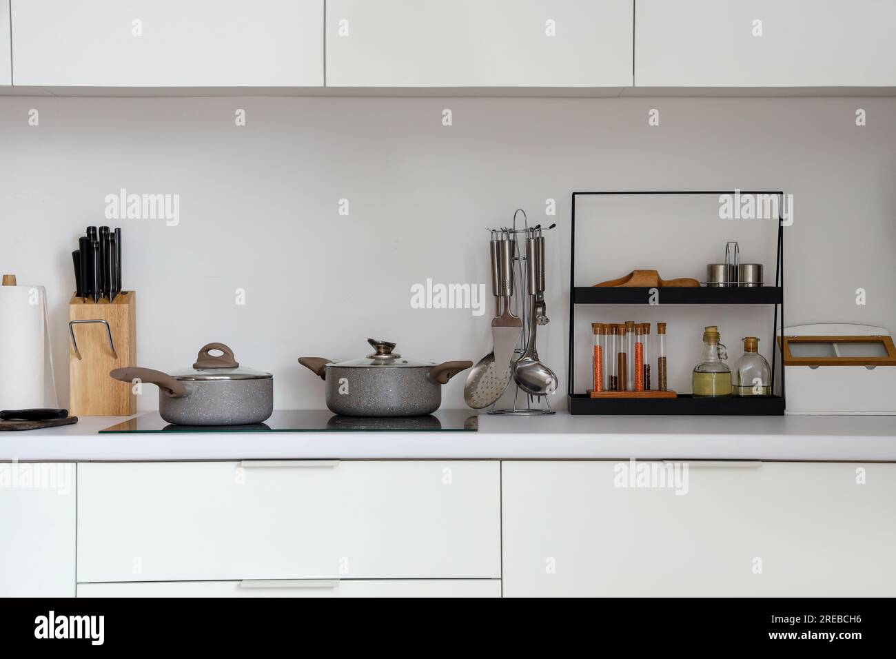White kitchen counters with electric stove, cooking pots and utensils