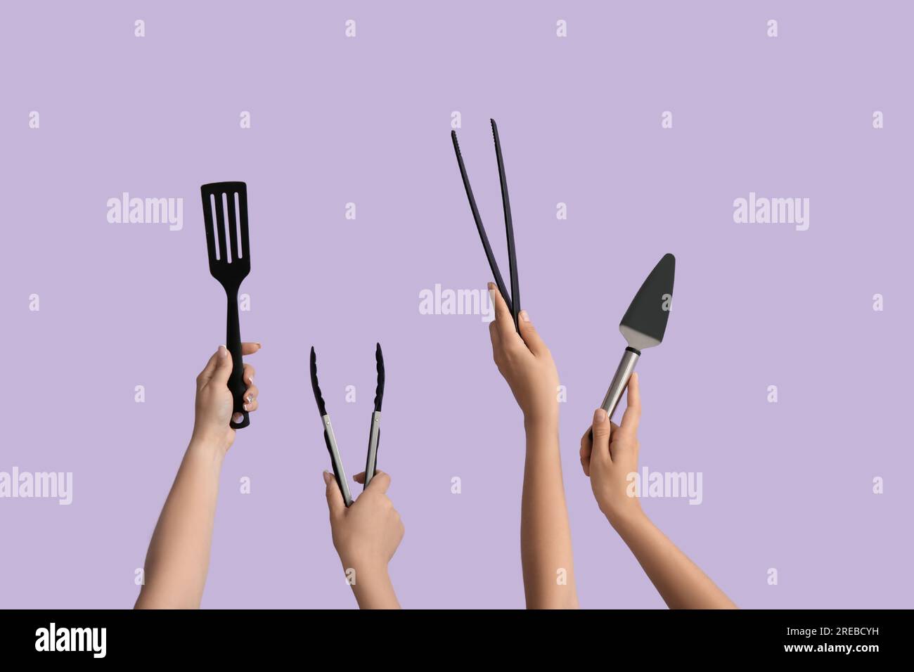 Female hands with tongs and spatulas on lilac background Stock Photo