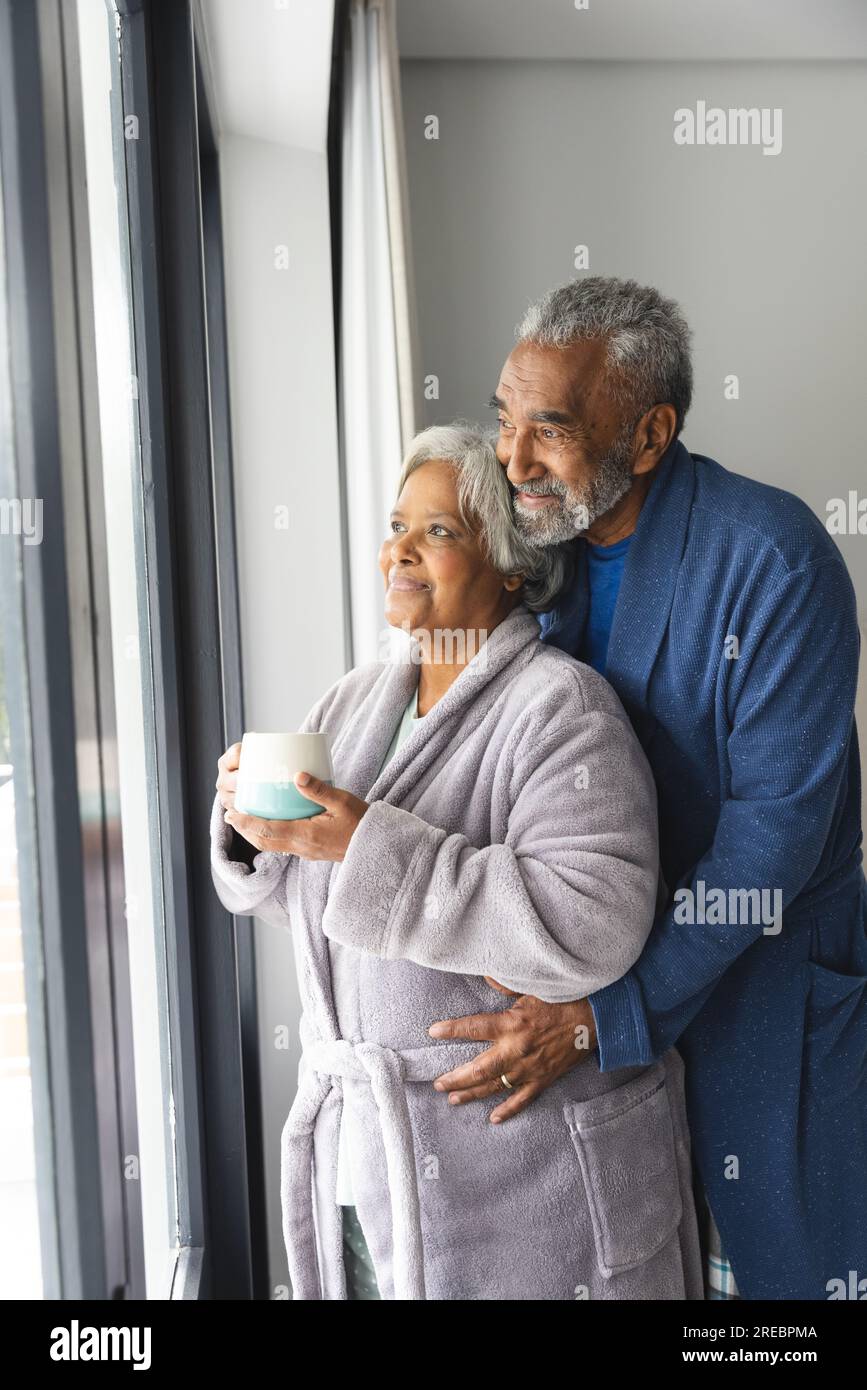 Happy senior biracial couple wearing bathrobes and looking through