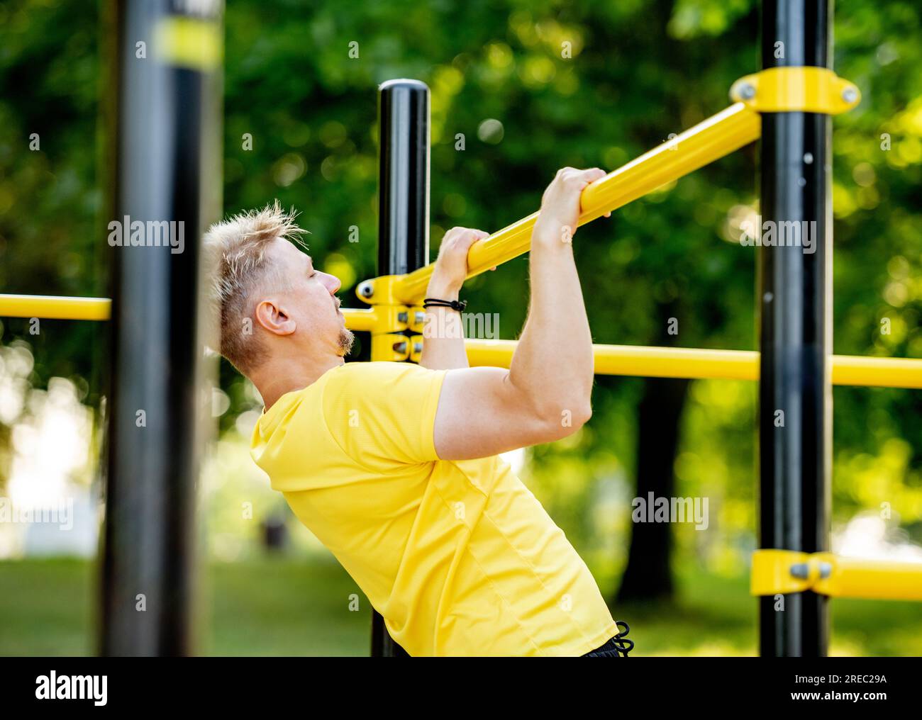 Man doing pull ups with horizontal bar outdoors in park for healthy