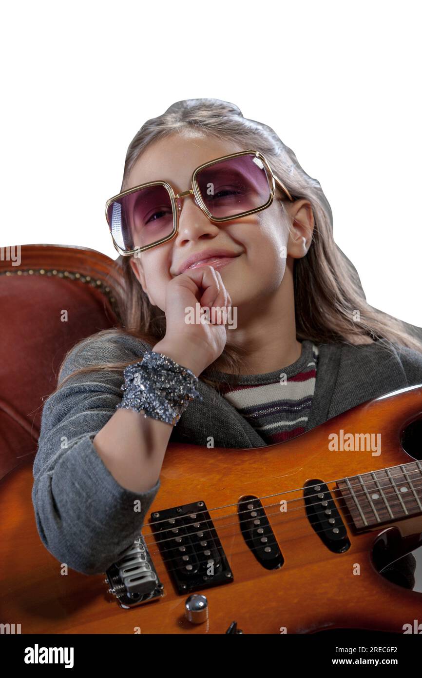 Imaginary pop-rock star, a young girl with an electric guitar, sunglasses, perched on a velvet baroque armchair, basking in adulation Stock Photo