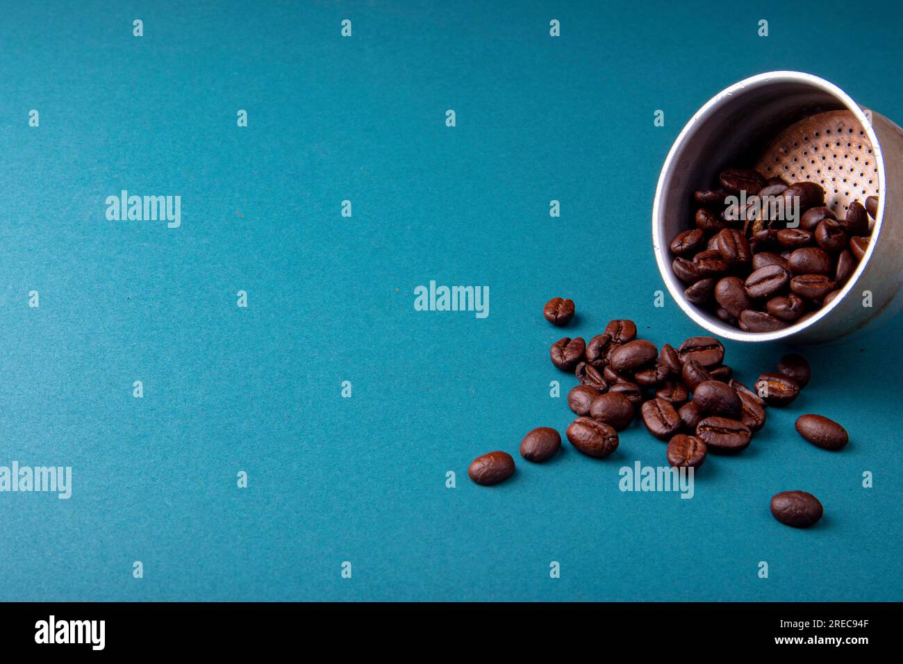 Aluminium filter with brown coffee beans on a teal blue surface with