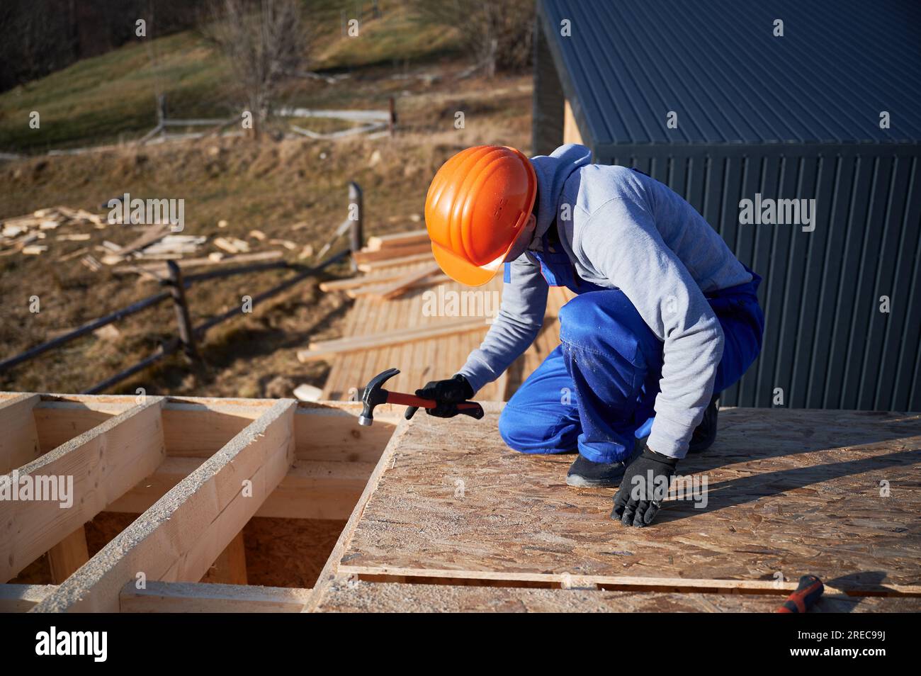 Carpenter hammering nail into OSB panel on the roof top of future