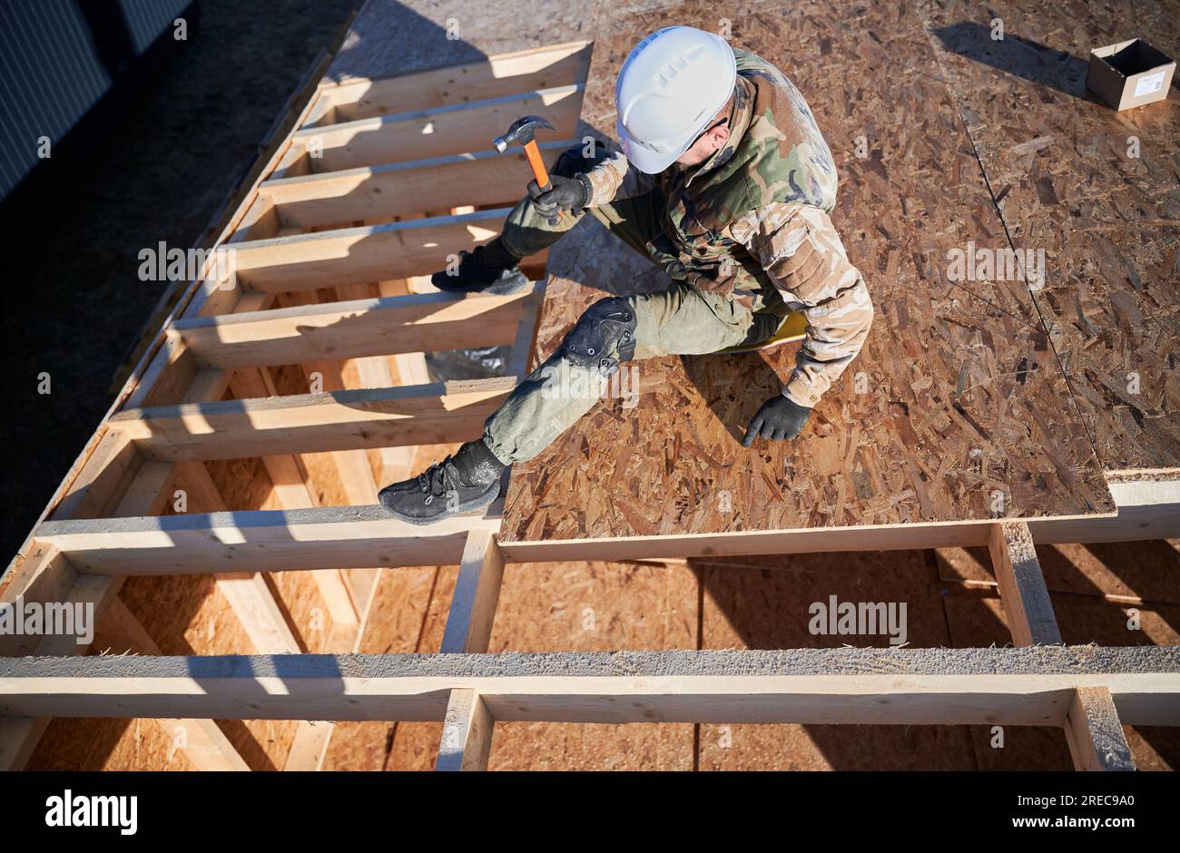 Carpenter hammering nail into OSB panel on the roof top of future