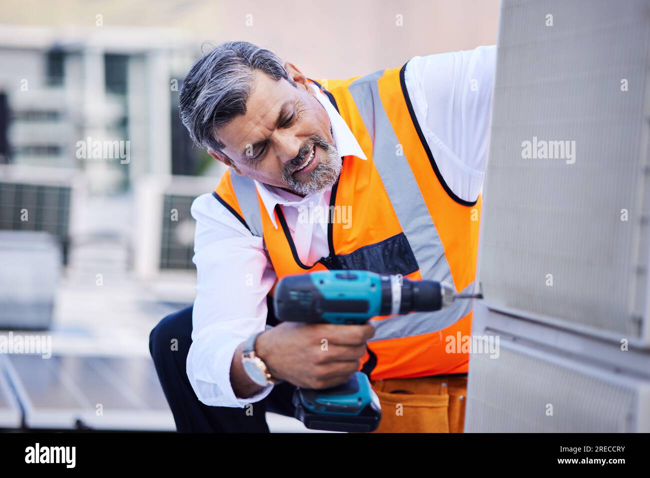 Solar panels, man and drill for building maintenance, renovation services or upgrade in city. Mature electrician, construction tools and engineering Stock Photo