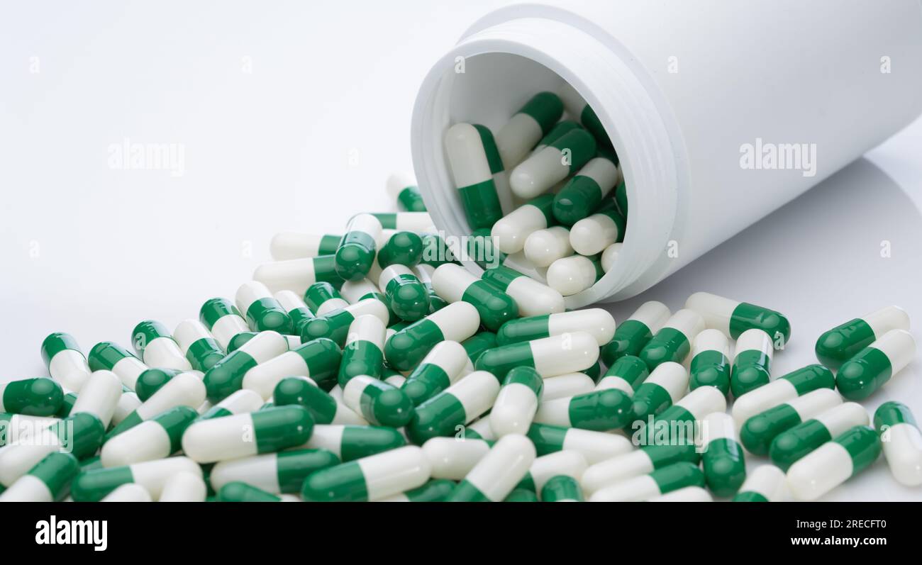 Green and white capsule pills spilled out of a white plastic bottle. Pharmaceutical industry. Prescription drug. Healthcare and medicine. Pharmacy Stock Photo