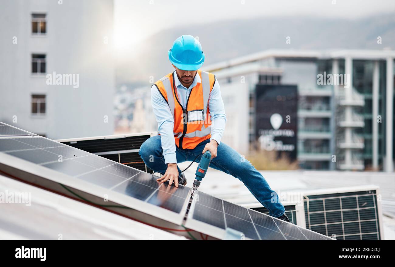 Technician man, drill and solar panel on roof with installation, sustainability and construction in city. Engineer, tools and photovoltaic system with Stock Photo
