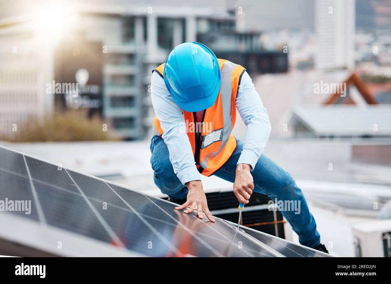 Engineer man, screwdriver and solar panel on roof for maintenance, industry and construction in city. Technician, tools and photovoltaic system with Stock Photo