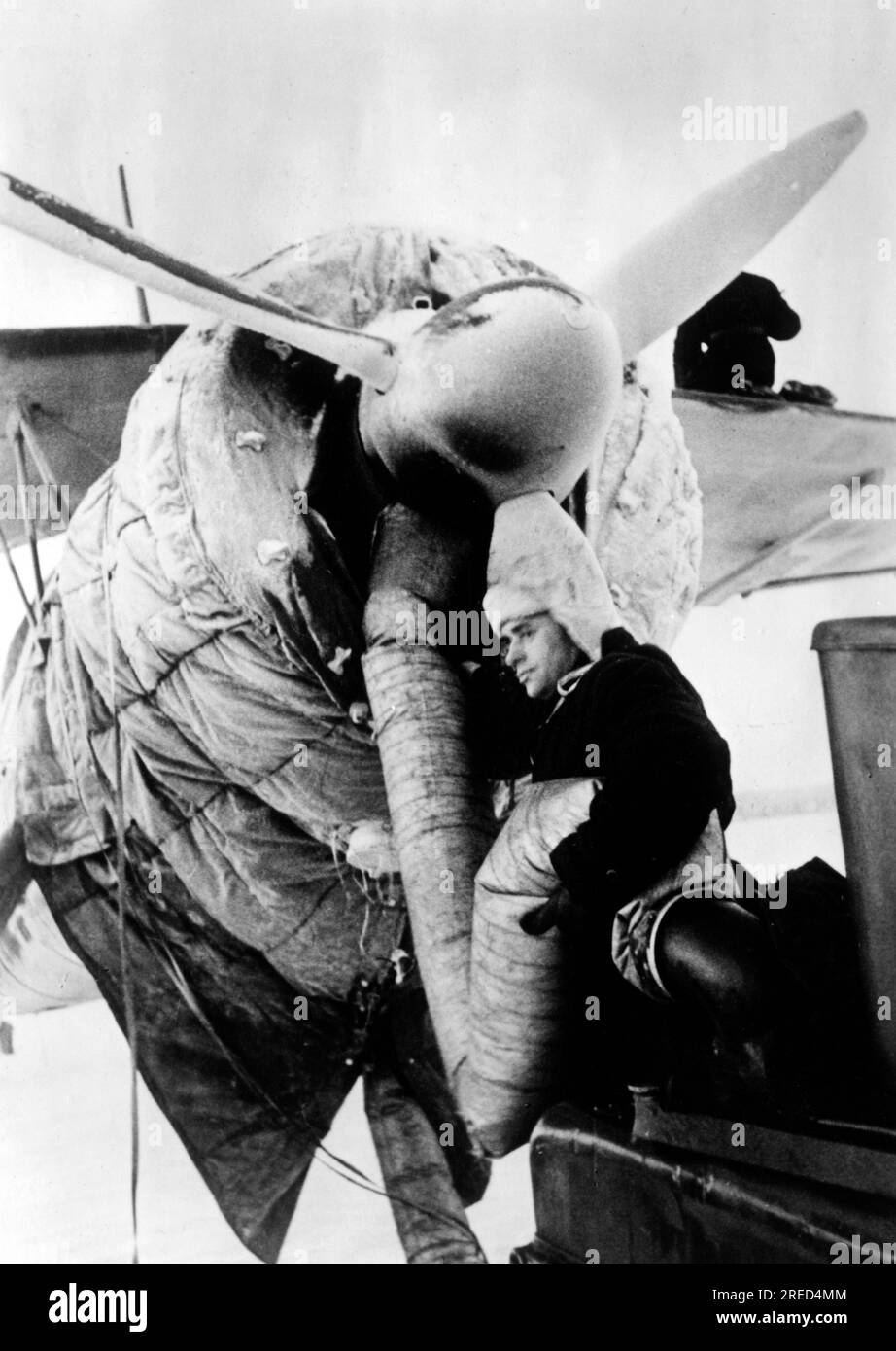 A soldier blows warm air into the engine of a Henschel Hs 126 with a hose to warm up the aircraft engine before takeoff. Photo: Speck. [automated translation] Stock Photo