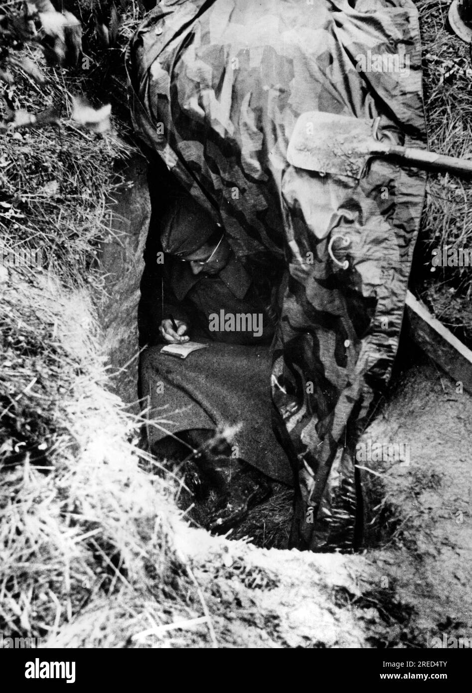 A soldier writes a letter in a hole in the ground on the Eastern Front