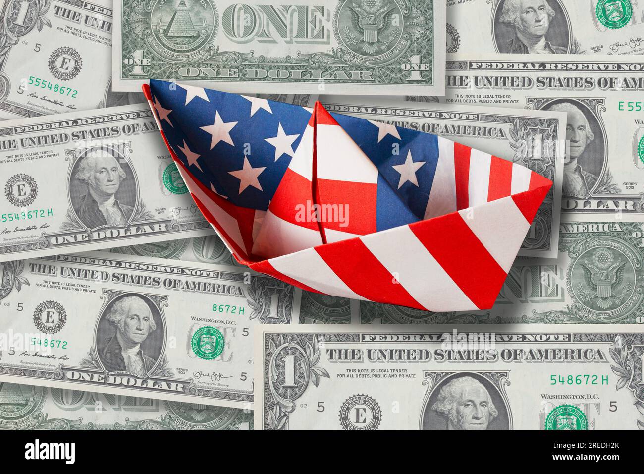 A pile of American one dollar banknotes with paper boat folded from US Stars and Stripes Flag. Stock Photo