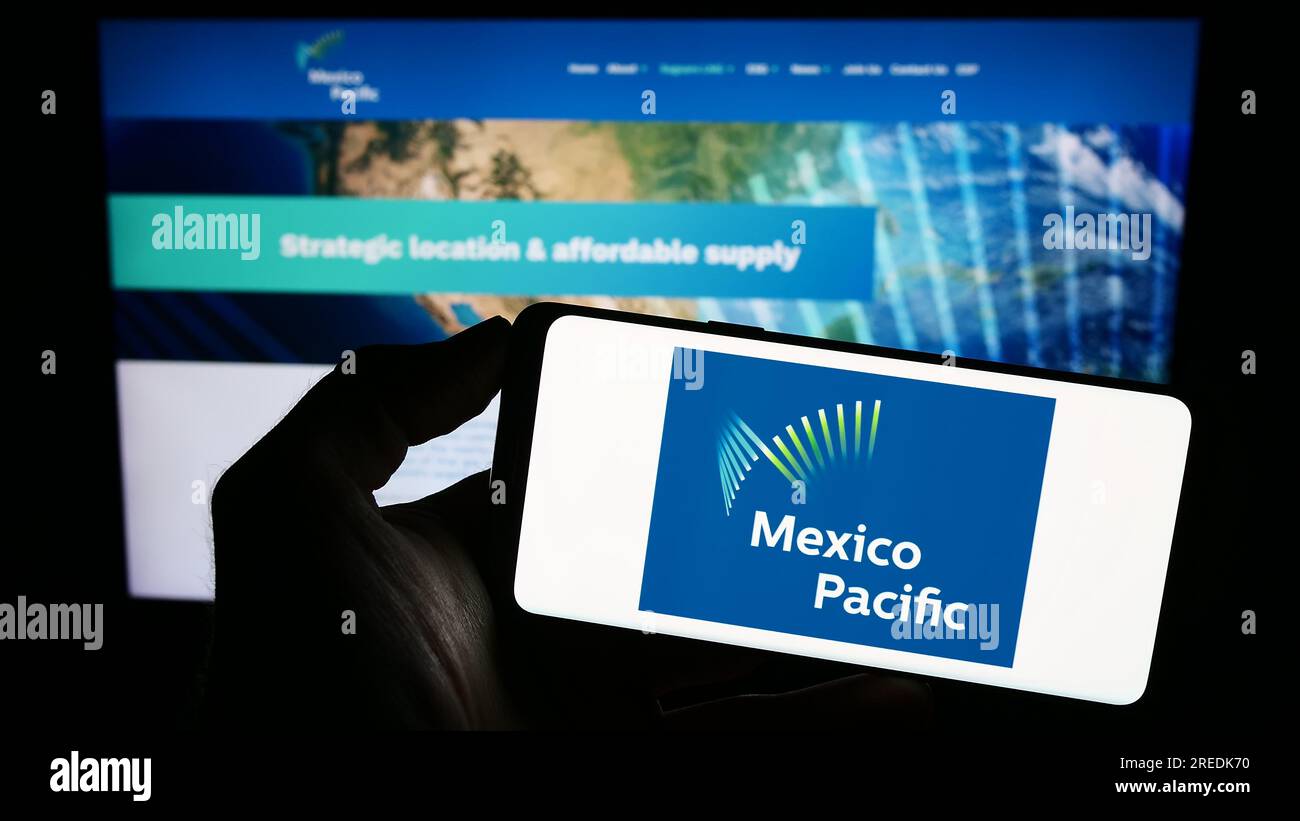 Person holding mobile phone with logo of company Mexico Pacific Ltd. LLC on screen in front of business web page. Focus on phone display. Stock Photo