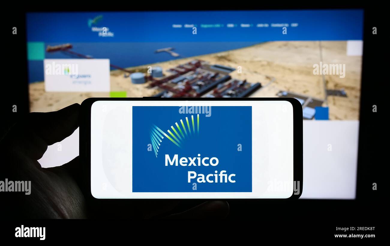 Person holding cellphone with logo of company Mexico Pacific Ltd. LLC on screen in front of business webpage. Focus on phone display. Stock Photo