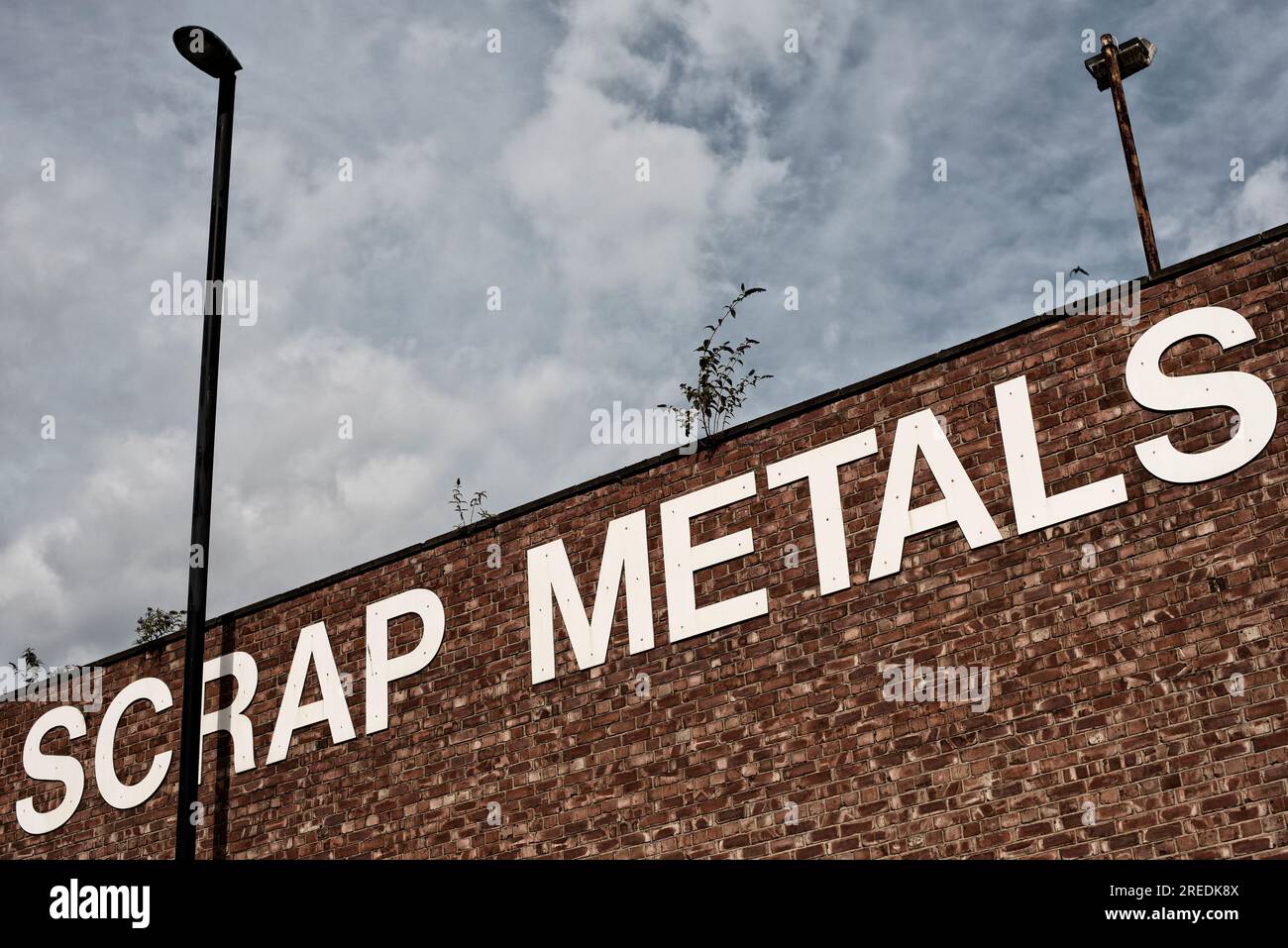 A sign for scrap metals in large white capital letter font on a red brick wall flanked by two lamp posts in Newcastle, England Stock Photo