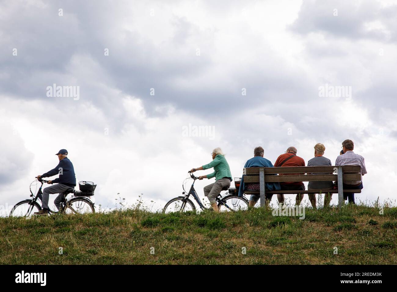 seniors sitting on a bench on the dike in Zons on the river Rhine, bicycle driver, North Rhine-Westphalia, Germany Senioren sitzen auf einer Bank auf Stock Photo