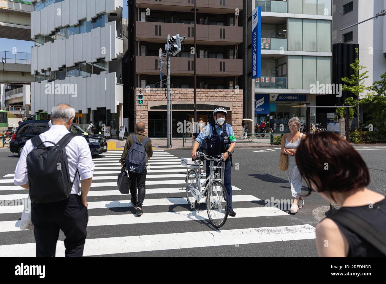 Japanese police officer pushes his bike over a crossroad near Tokyo Tower. Stock Photo