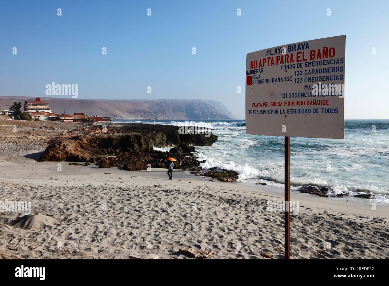 Dangerous beach, bathing prohibited sign with emergency contact phone numbers at Playa Brava on Pacific coast just south of Arica, Chile Stock Photo