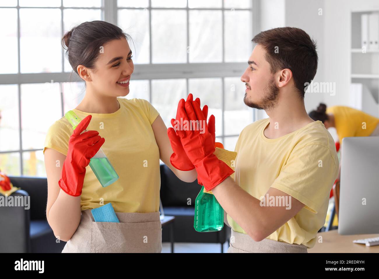 Young janitors with bottles of detergent giving each other highfive in